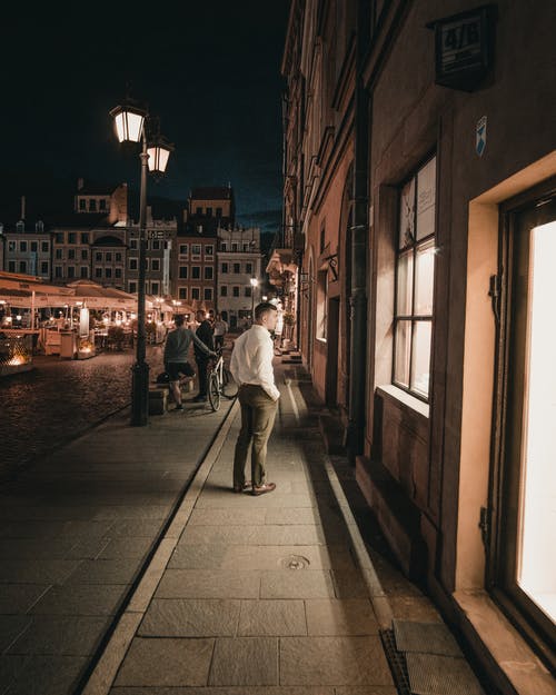 白衬衫和棕色的裤子，在夜间在人行道上行走的人 · 免费素材图片