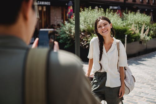 拍摄智能手机在城市街道上的匿名家伙快乐亚洲女友 · 免费素材图片