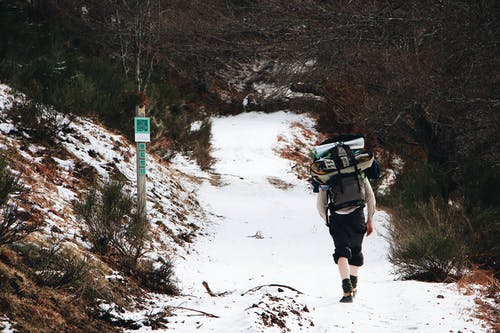 黑裤子的人背着背包走在积雪的地面上 · 免费素材图片
