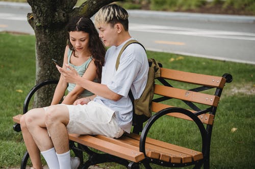 年轻时尚多种族夫妇在公园里的智能手机上观看视频 · 免费素材图片