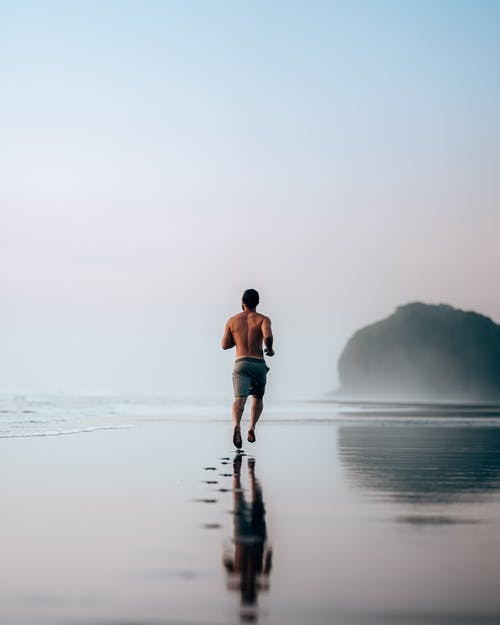 在湿的风景秀丽的海滨上慢跑的匿名肌肉男 · 免费素材图片