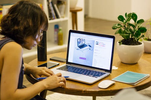 面对黑色的手提电脑，棕色木制圆桌上的黑色背心衬衫的女人 · 免费素材图片
