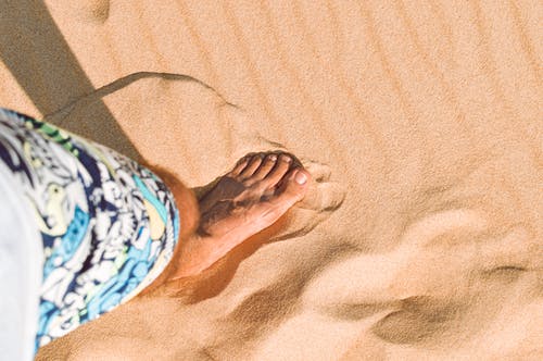 蓝色和白色的花短裤，站在棕色沙滩上的人 · 免费素材图片