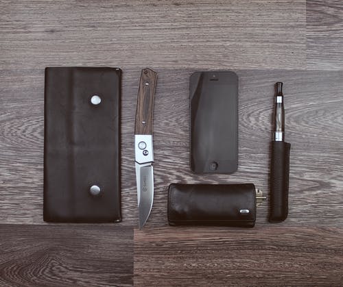 棕色木质表面上的棕色刀，黑色iphone 5和黑色蒸发器笔 · 免费素材图片