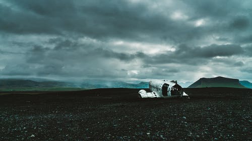 飞机残骸在灰色多云的天空下的黑沙 · 免费素材图片