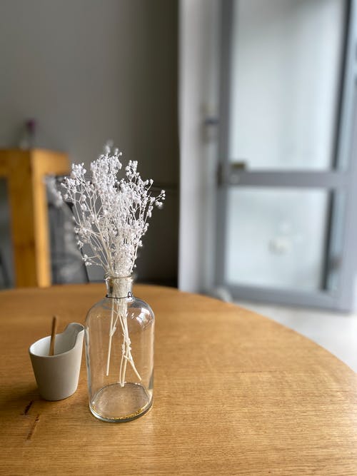 在透明的玻璃花瓶，棕色木制的桌子上的白花 · 免费素材图片