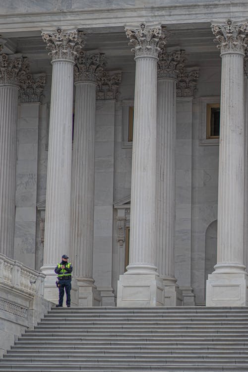 一名警官站在建筑物的白色混凝土柱子附近 · 免费素材图片