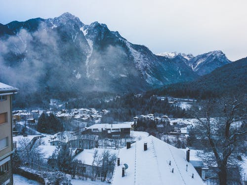 在晴朗的天空下的白雪覆盖的山附近的积雪的房子 · 免费素材图片