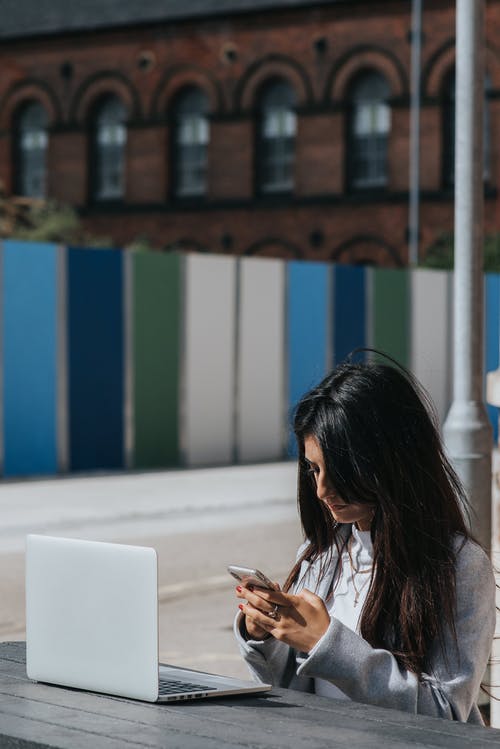 在智能手机上聊天在桌上的笔记本电脑的族裔女企业家 · 免费素材图片