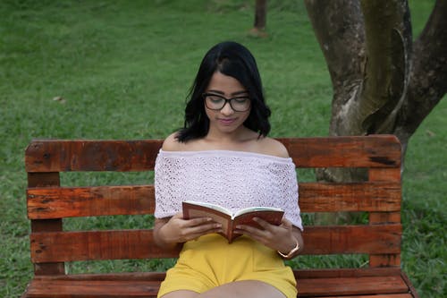 女人坐在木凳上看书 · 免费素材图片