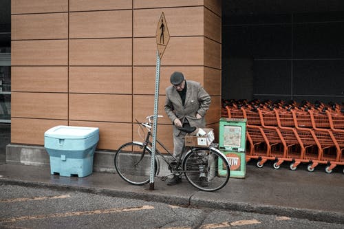 男子在棕墙附近停车一辆自行车 · 免费素材图片