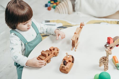 玩棕色木制玩具的白色和绿色的长袖衬衫的男孩 · 免费素材图片