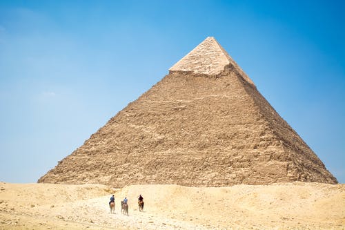 人们骑着骆驼在蓝蓝的天空下金字塔附近 · 免费素材图片