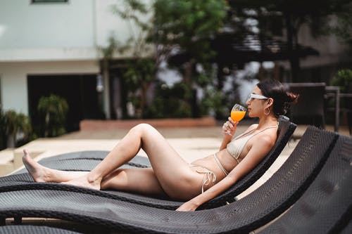 自信的年轻民族女性喝果汁，在度假村的日光浴浴床上休息 · 免费素材图片