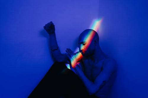 裸照的人坐在蓝灯室墙附近 · 免费素材图片