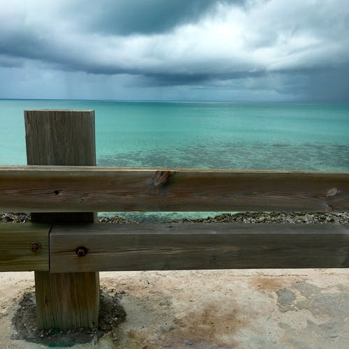 白天在多云的蓝天下蓝色海洋水附近的棕色木栅栏 · 免费素材图片