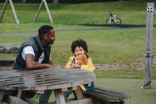 性格开朗的黑人父亲和儿子坐在公园的桌旁 · 免费素材图片