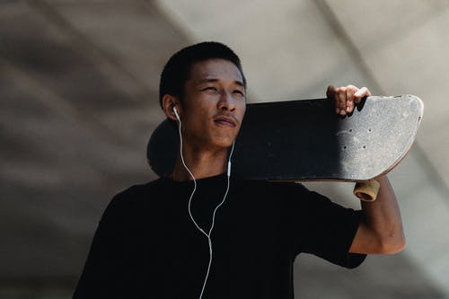 亚洲的年轻人，带着耳机和滑板 · 免费素材图片