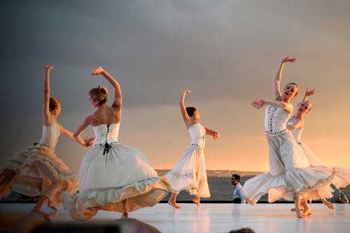 5名穿着白色连衣裙的妇女在日落时分在灰色的天空下跳舞 · 免费素材图片