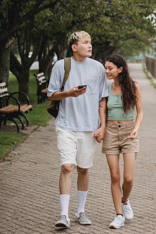 恩爱的夫妻，沿着公园的小巷里散步，使用智能手机 · 免费素材图片