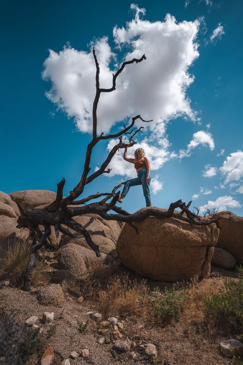 抹胸和牛仔牛仔裤，站在棕色的岩石，在蓝蓝的天空下的女人 · 免费素材图片