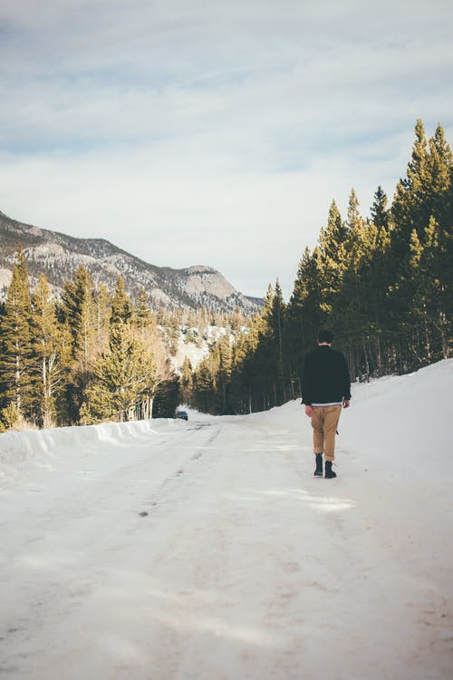黑夹克和棕色的裤子，在积雪覆盖的田野上行走的人 · 免费素材图片