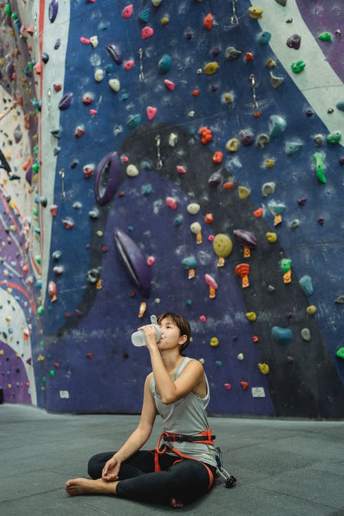 女运动员在攀岩墙和饮用水附近的地板上休息 · 免费素材图片