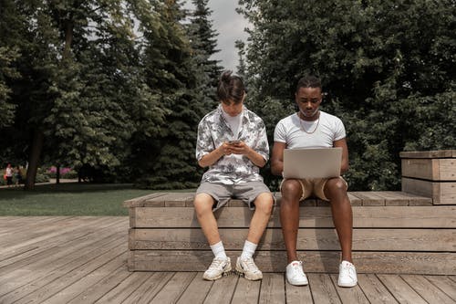 集中使用智能手机和上网本坐在公园的长椅上的不同年轻人 · 免费素材图片