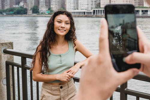 无法识别的人拍摄微笑智能手机在路堤上的族裔女性朋友 · 免费素材图片