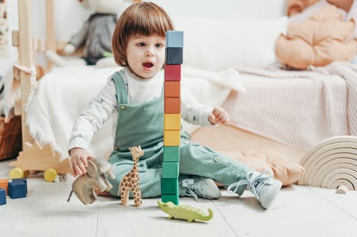 白色的长袖上衣和绿色的粗蓝布长裤的孩子玩乐高积木和玩具 · 免费素材图片