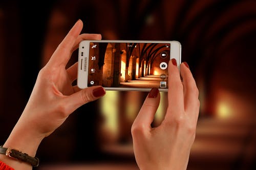 女人抱着一个白色的三星galaxy Android智能手机拍照的走廊 · 免费素材图片