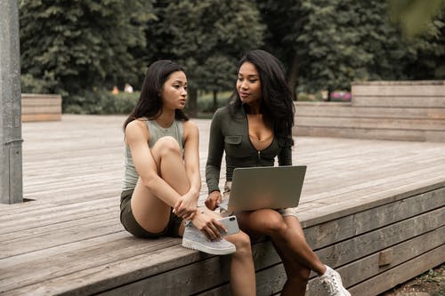 严重的年轻多种族女士共享笔记本电脑和在公园聊天 · 免费素材图片