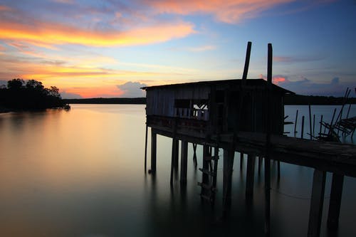 在日落期间在海水上的房子的轮廓 · 免费素材图片