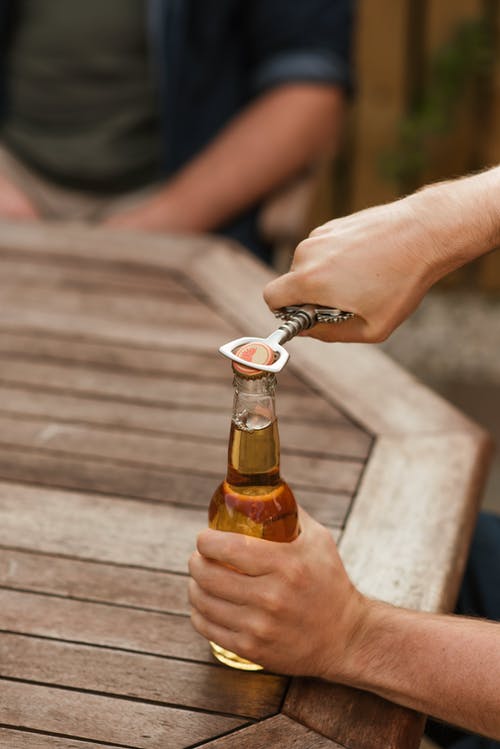 男子脱开啤酒瓶盖与开瓶器 · 免费素材图片