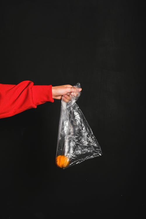 红色长袖上衣的人拿着里面的无色塑料袋和黄色水果 · 免费素材图片