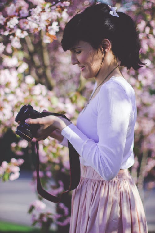 白色长袖上衣和粉红色的裙子，拿着黑色的单反相机的女人 · 免费素材图片