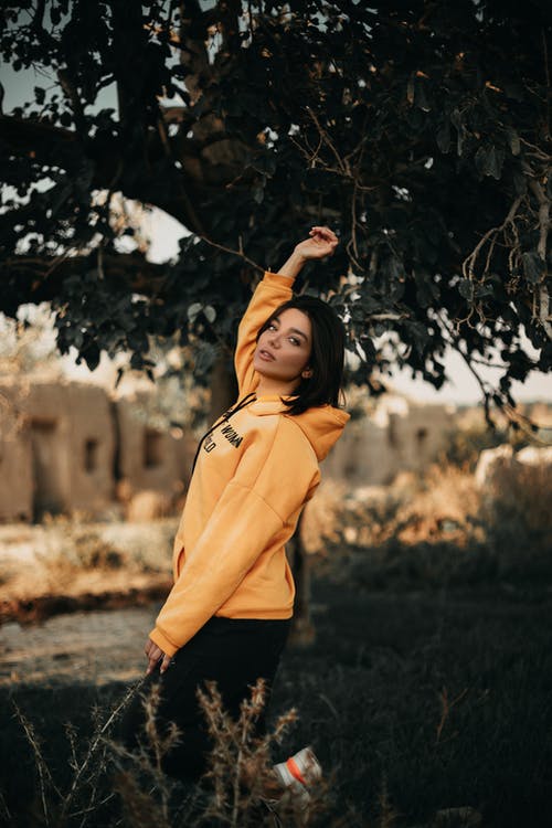穿黄色连帽衫站在树旁边的女人 · 免费素材图片