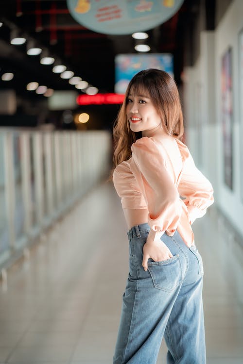 米色的长袖衬衫和蓝色牛仔牛仔裤，站在走廊上的女人 · 免费素材图片