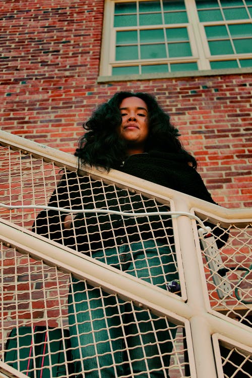 黑色外套站在棕色砖墙旁边的女人 · 免费素材图片