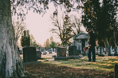 穿黑夹克的男人站在坟墓前 · 免费素材图片