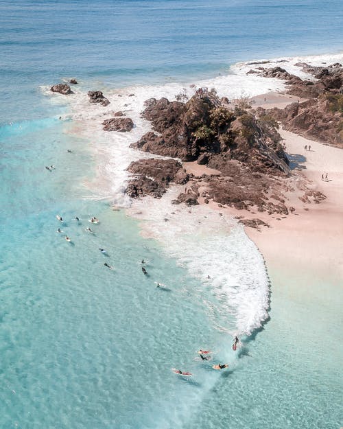 无法识别的游客在岩石海岸附近的海洋中游泳 · 免费素材图片