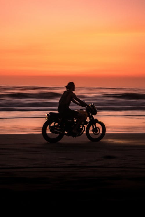 男子在日落海滩上骑摩托车 · 免费素材图片