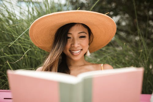 微笑的女人，戴着太阳帽和看书 · 免费素材图片