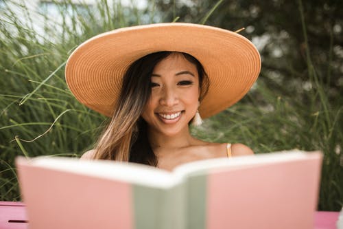 微笑的女人，戴着太阳帽和看书 · 免费素材图片