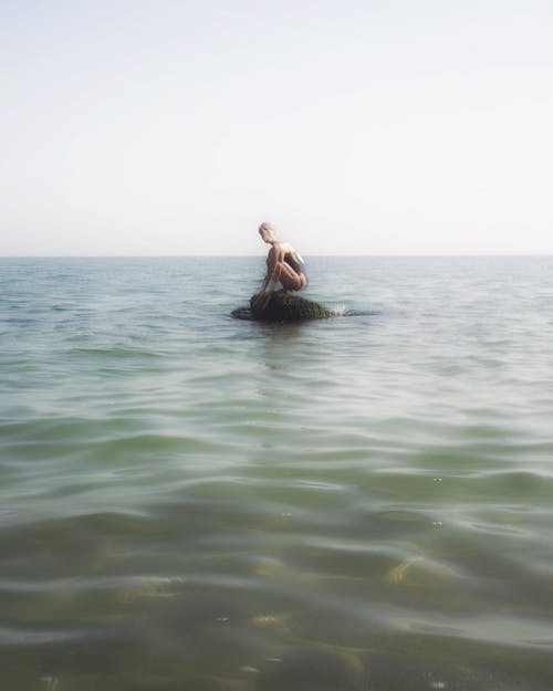 女人坐在海中的一块岩石上 · 免费素材图片