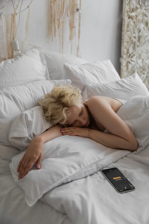 躺在床上，闹钟在智能手机上的困女人 · 免费素材图片