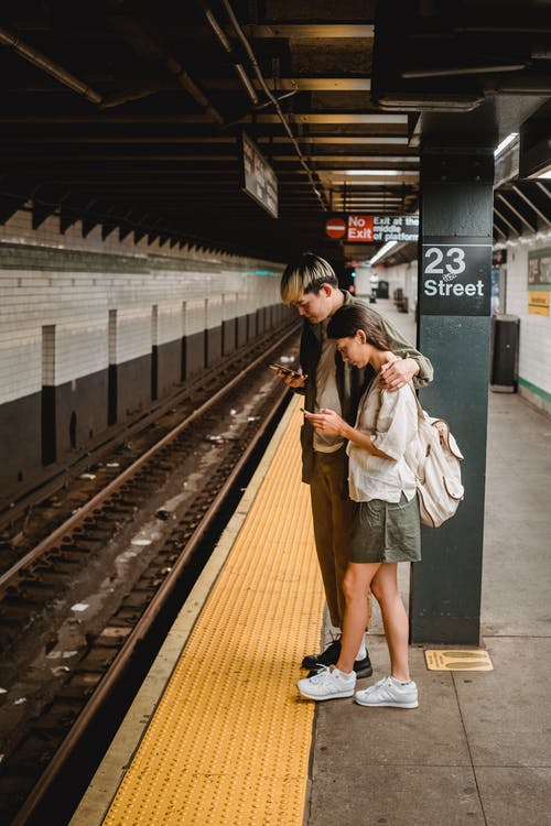 集中亚洲夫妇在地铁站中使用手机 · 免费素材图片