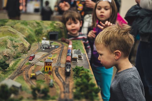 男孩站在微型火车玩具附近的选择性焦点照片 · 免费素材图片