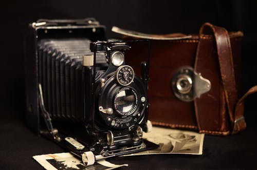 黑色经典相机，棕色皮包附近 · 免费素材图片