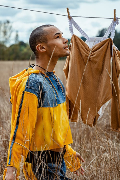 男人穿着黄色和蓝色外套站在棕色的原野上 · 免费素材图片